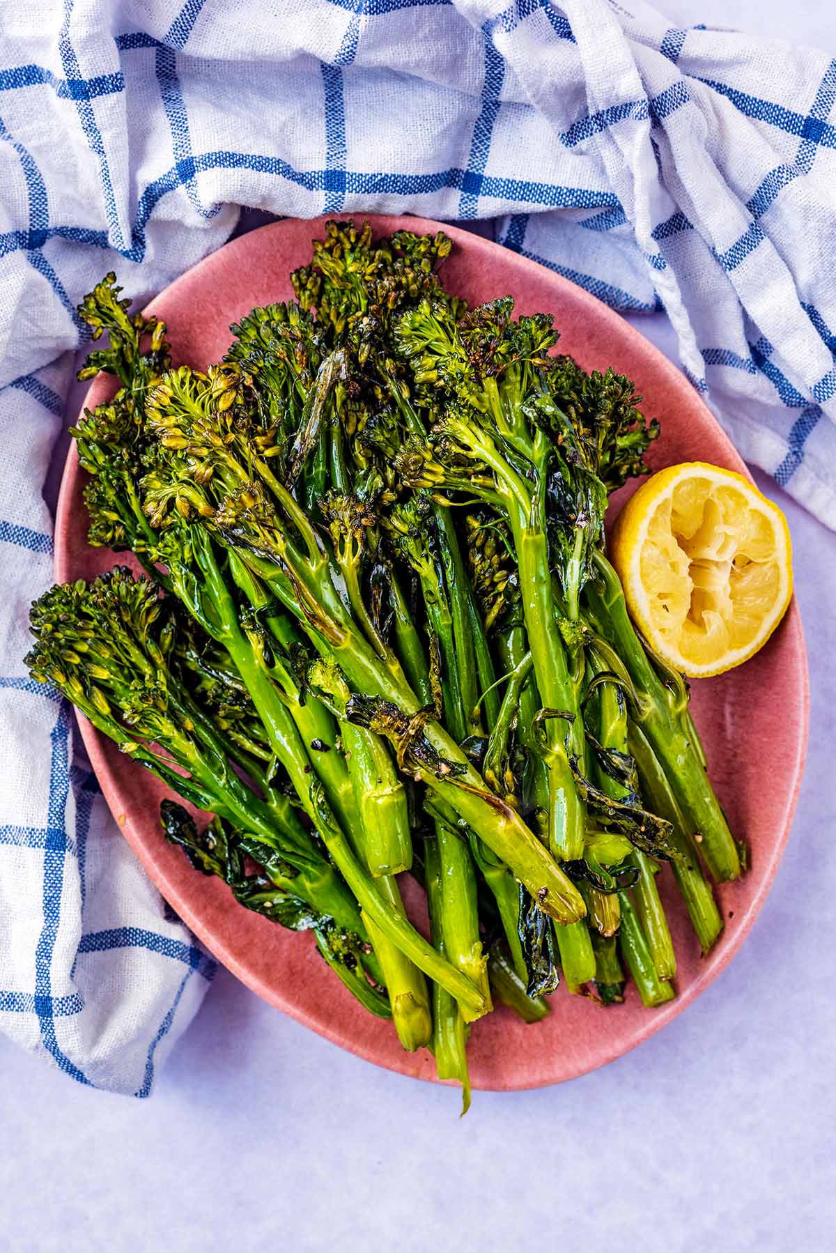 An oval bowl filled with roasted broccoli and a lemon half.