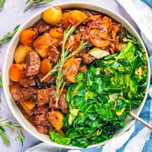 A bowl of beef bourguignon with some cooked greens.
