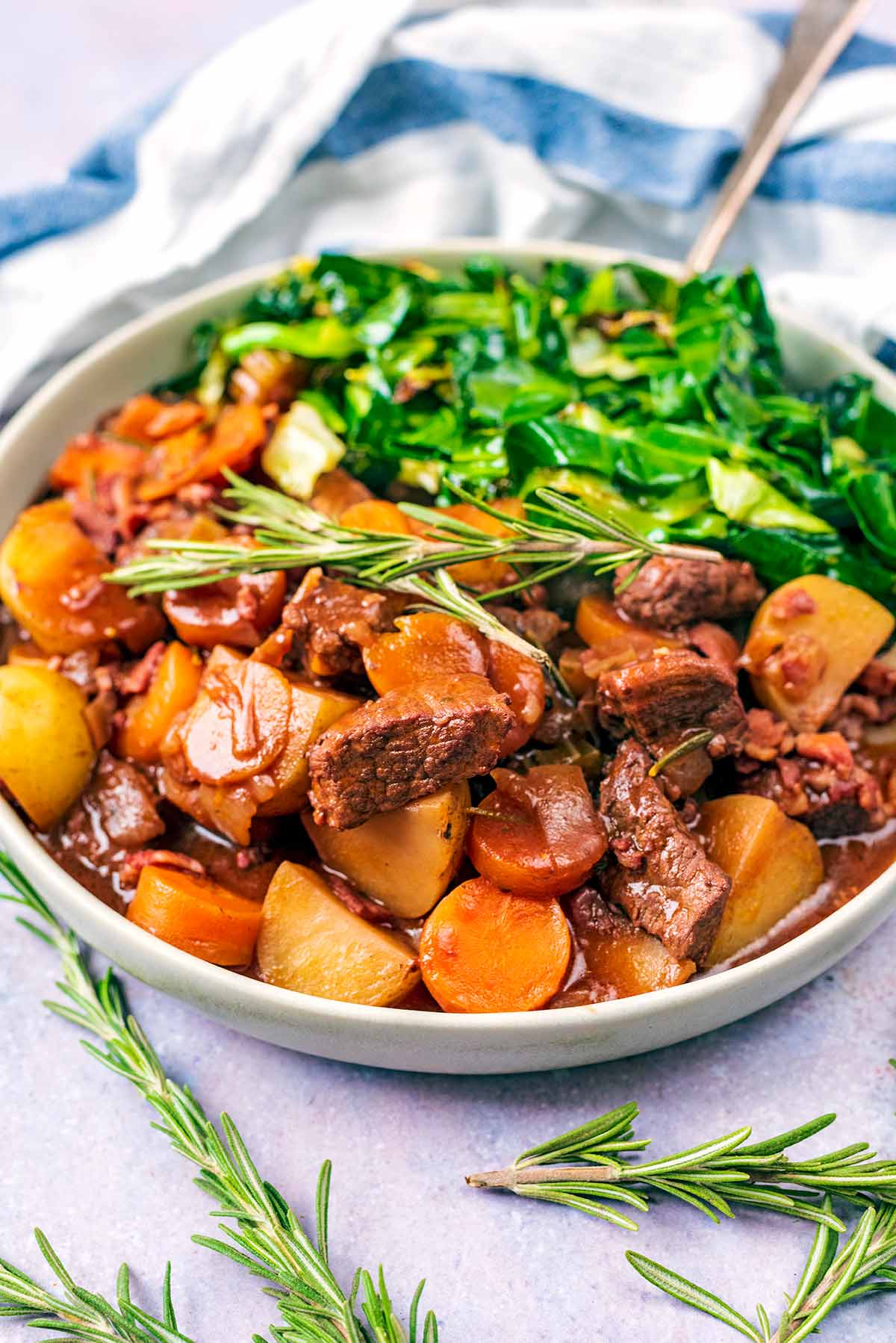 Beef bourguignon and cooked greens in a bowl in front of a blue and white towel.