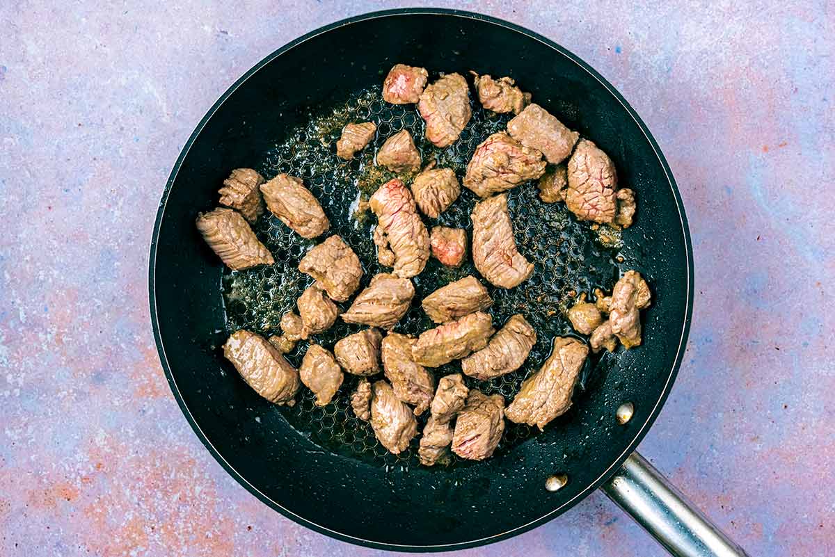 Chunks of beef browning in a frying pan.