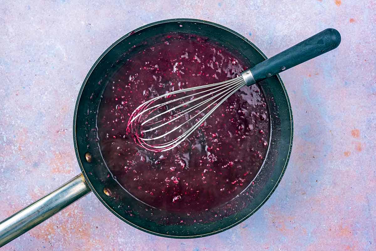 The pan being deglazed with red wine. A whisk is in the pan.