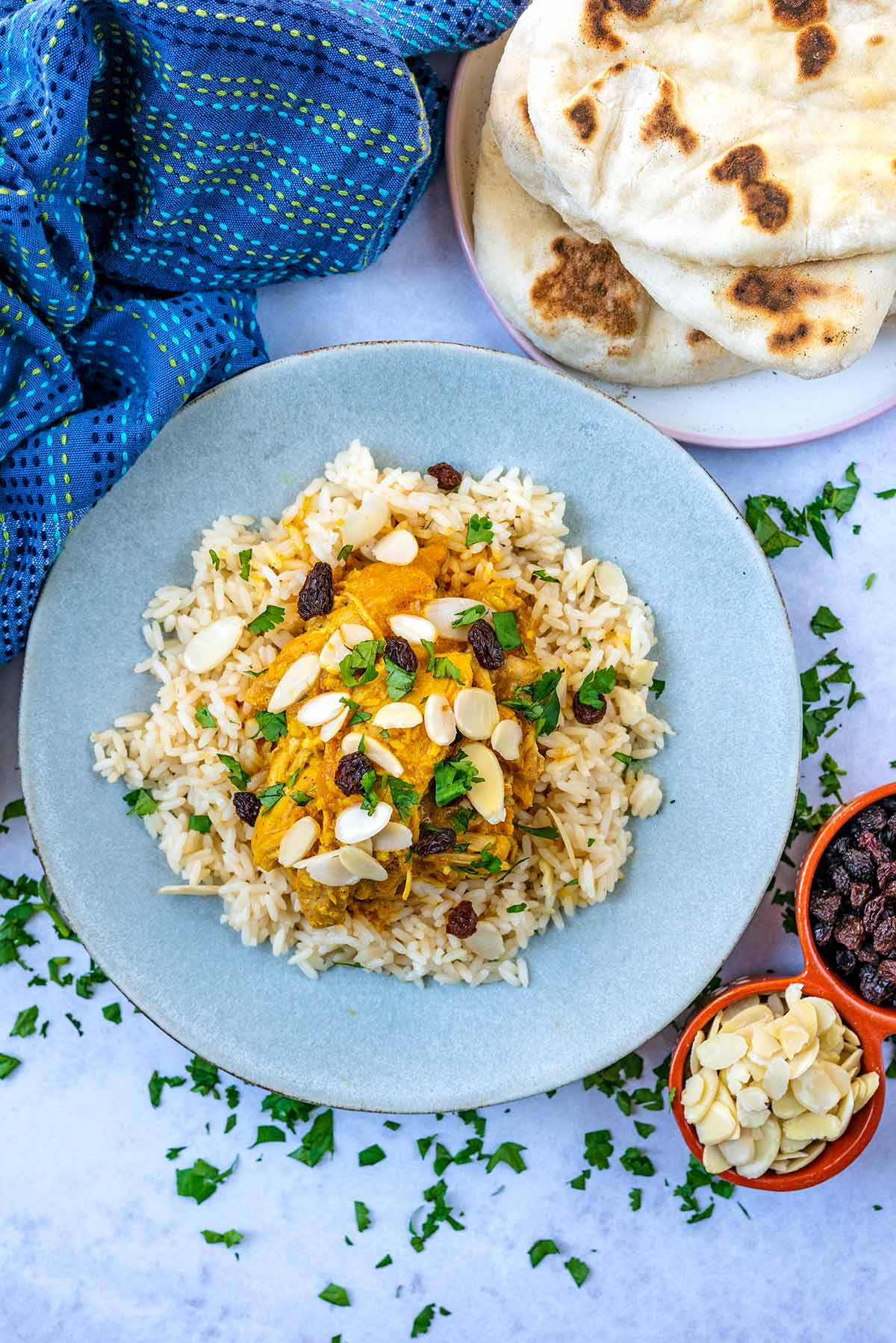 A plate of chicke korma and rice next to some naan breads and a bowl of flaked almonds.