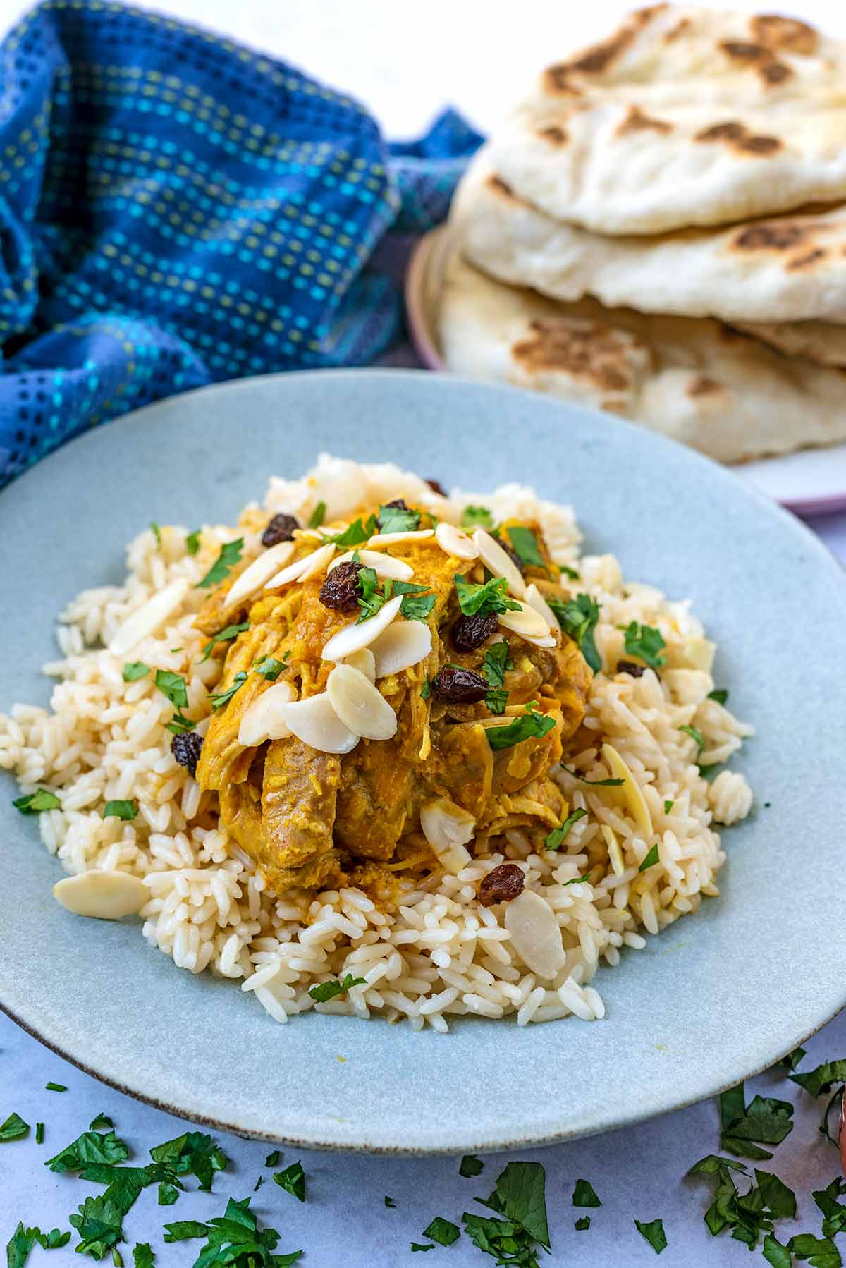 A plate of chicken korma and rice in front of some naan breads.