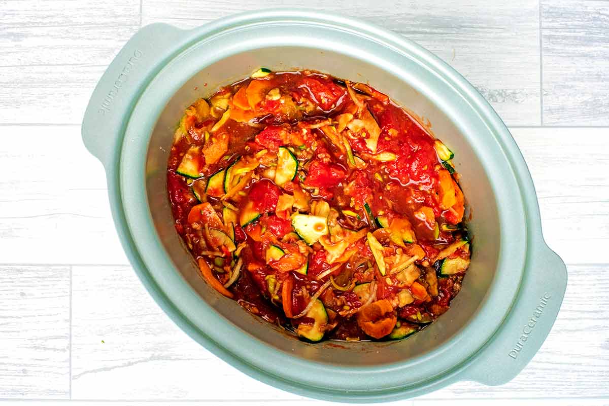 Slow cooker bowl containing chopped vegetables and tomato sauce.