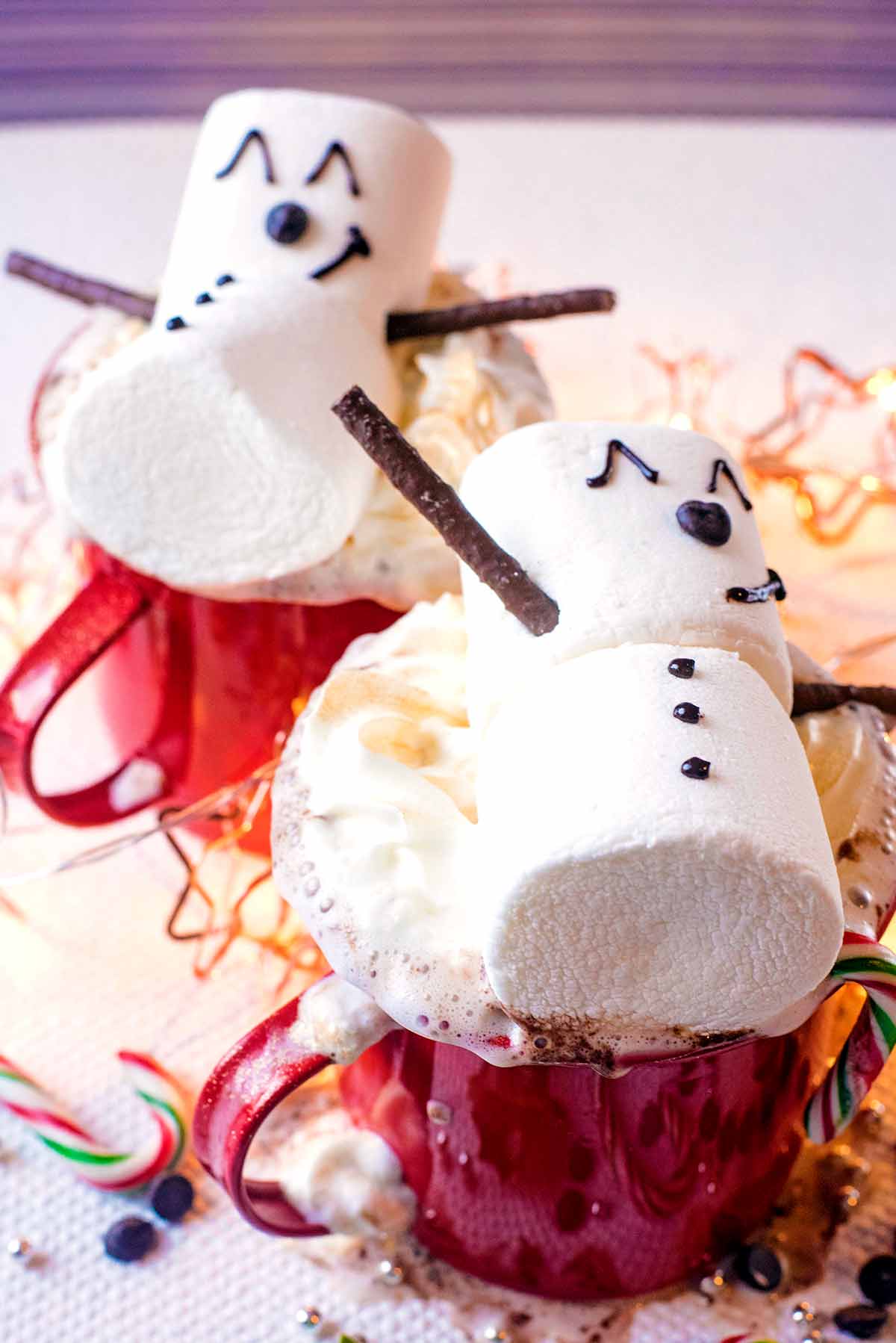 Two mugs of hot chocolate topped with cream and decorated with snowman marshmallows.