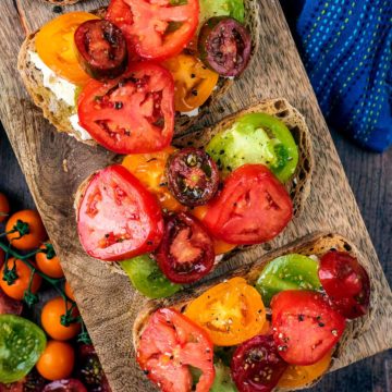Tomatoes on toast on a wooden serving board.