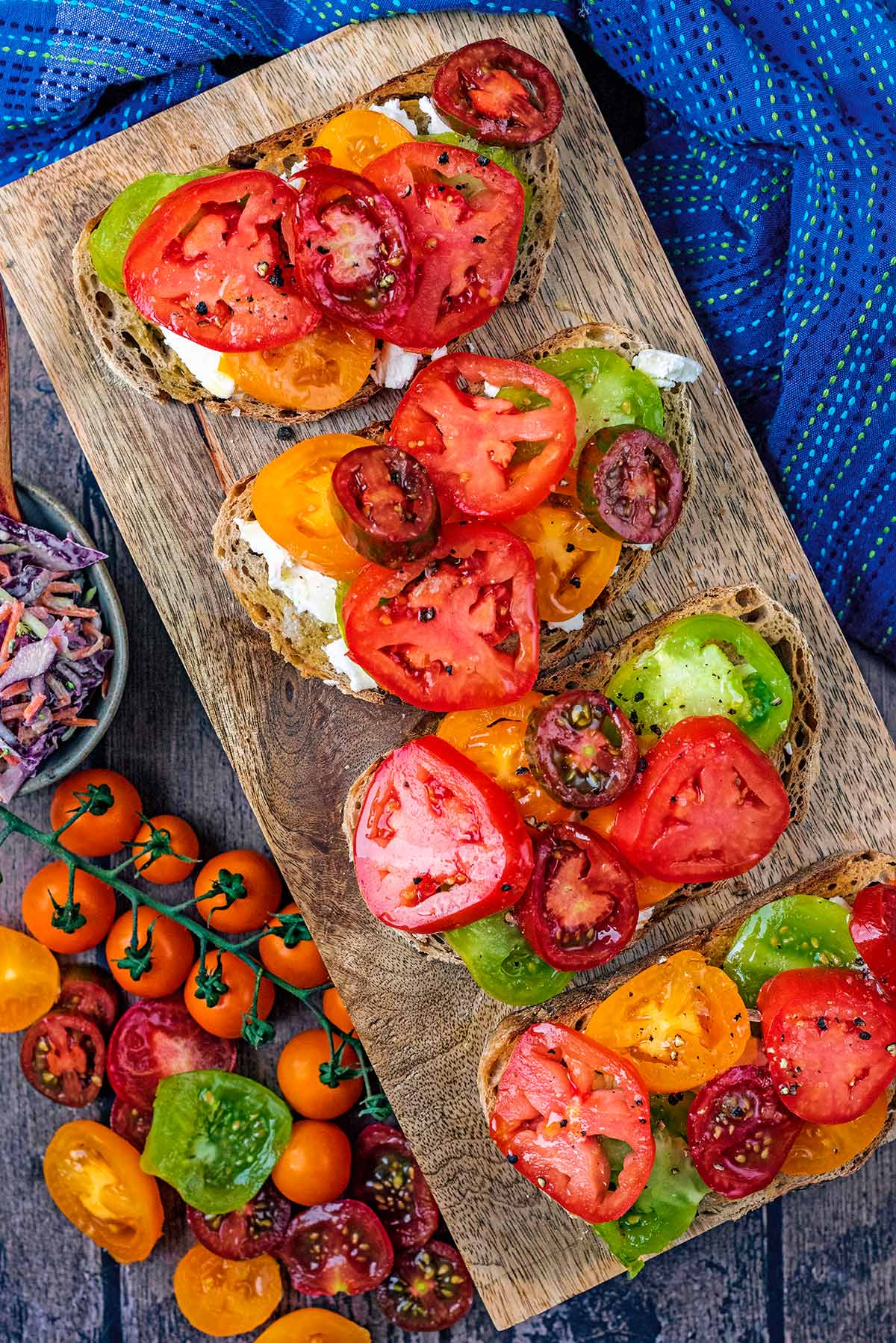 A wooden serving board with four slices of tomato topped toast.