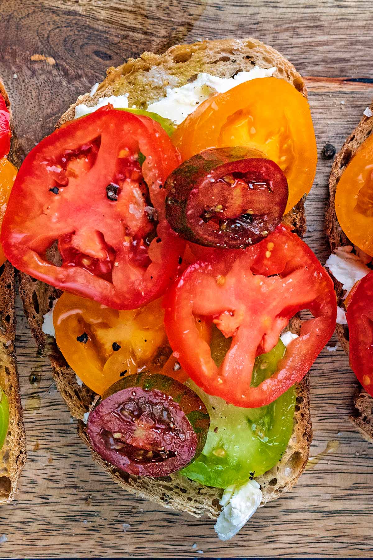 Red, green and yellow tomato slices on top of a slice of toasted bread.