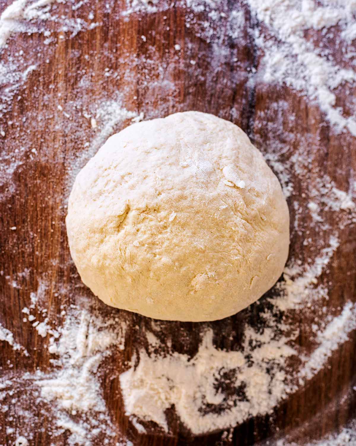 A ball of kneaded bread dough on a wooden surface.