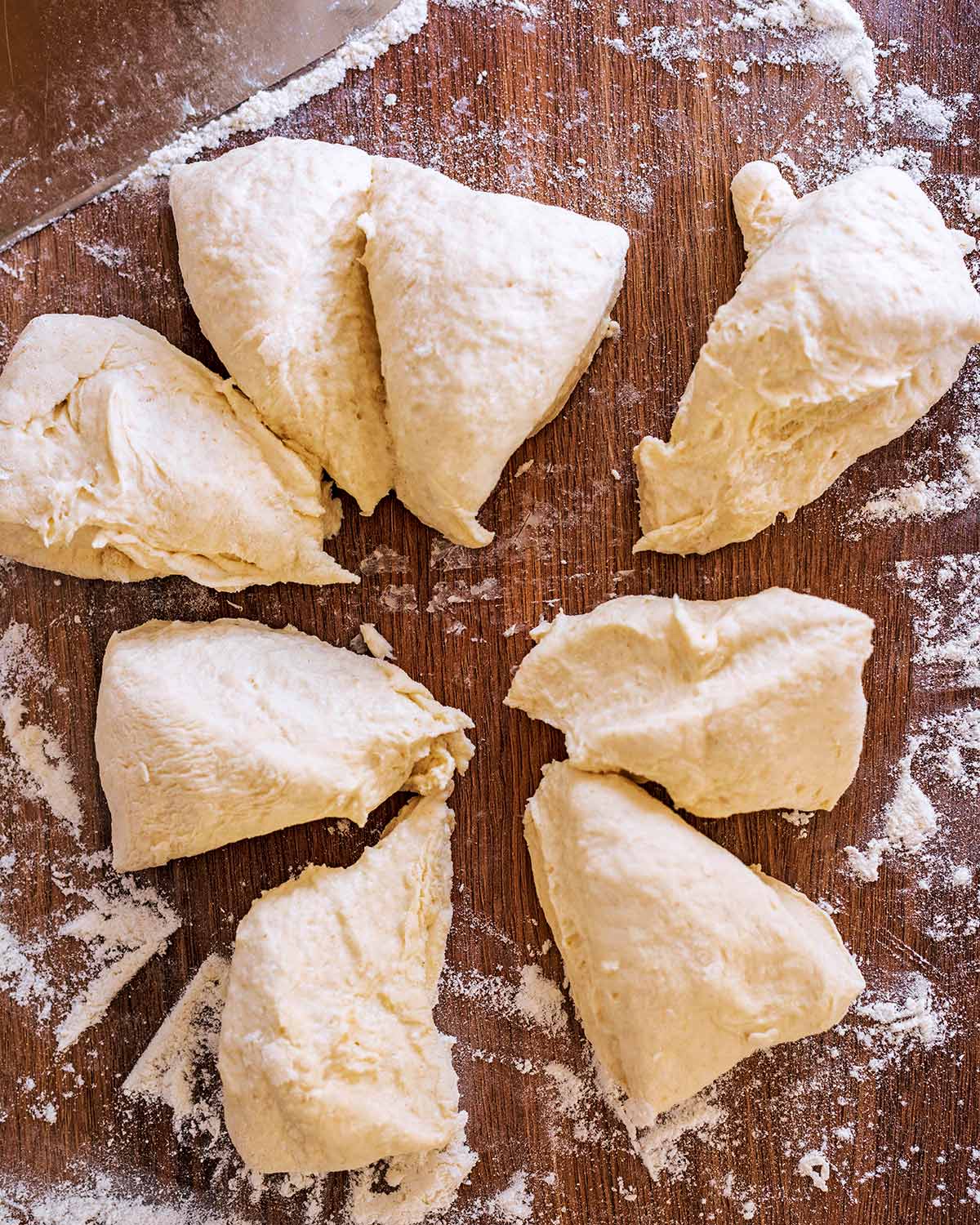 Eight pieces of bread dough on a wooden surface.