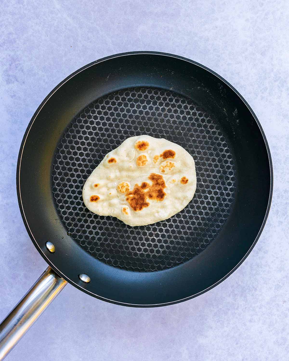 A slightly charred naan bread frying in a pan.