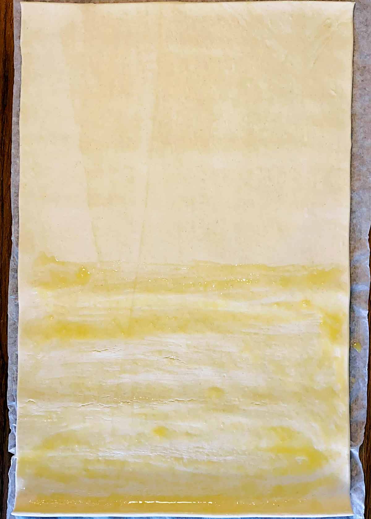 A sheet of puff pastry with half of it covered in egg wash.