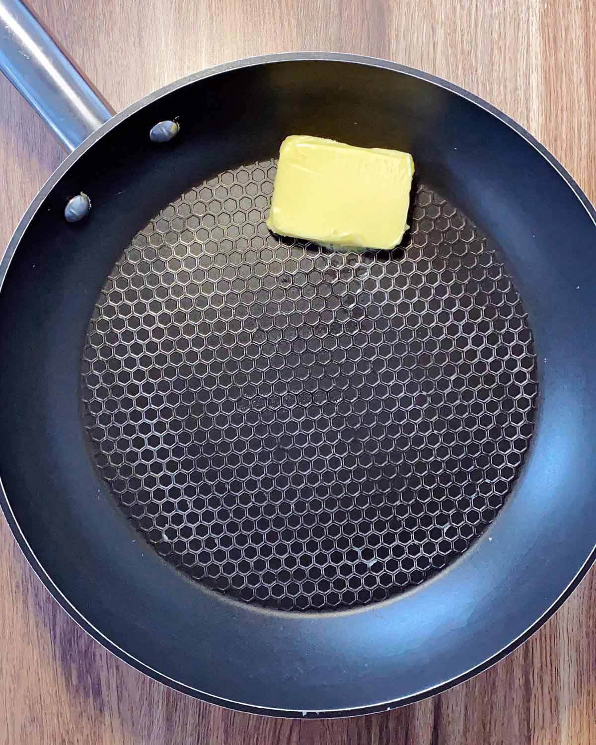 A pat of butter melting in a black frying pan.