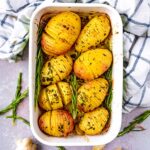 Eight hasselback potatoes in a baking dish with sprigs of rosemary.
