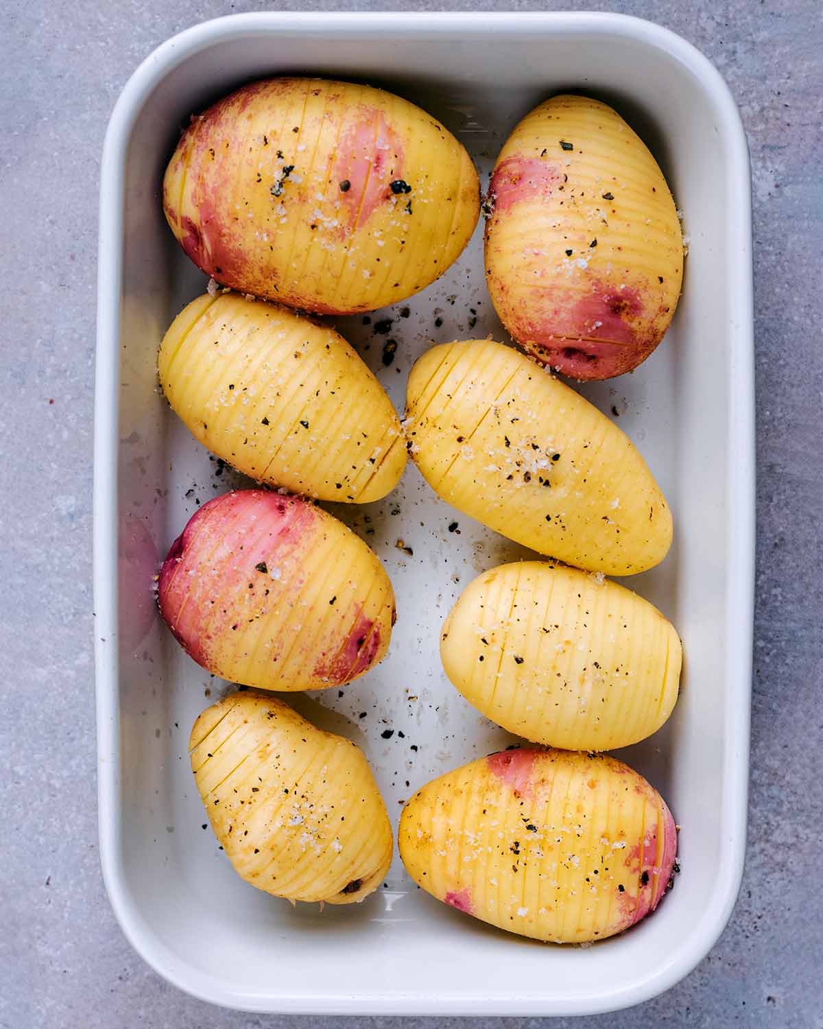 Uncooked hasselback potatoes in a white baking dish.