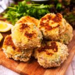 Salmon fishcakes on a wooden serving board with salad in the background.