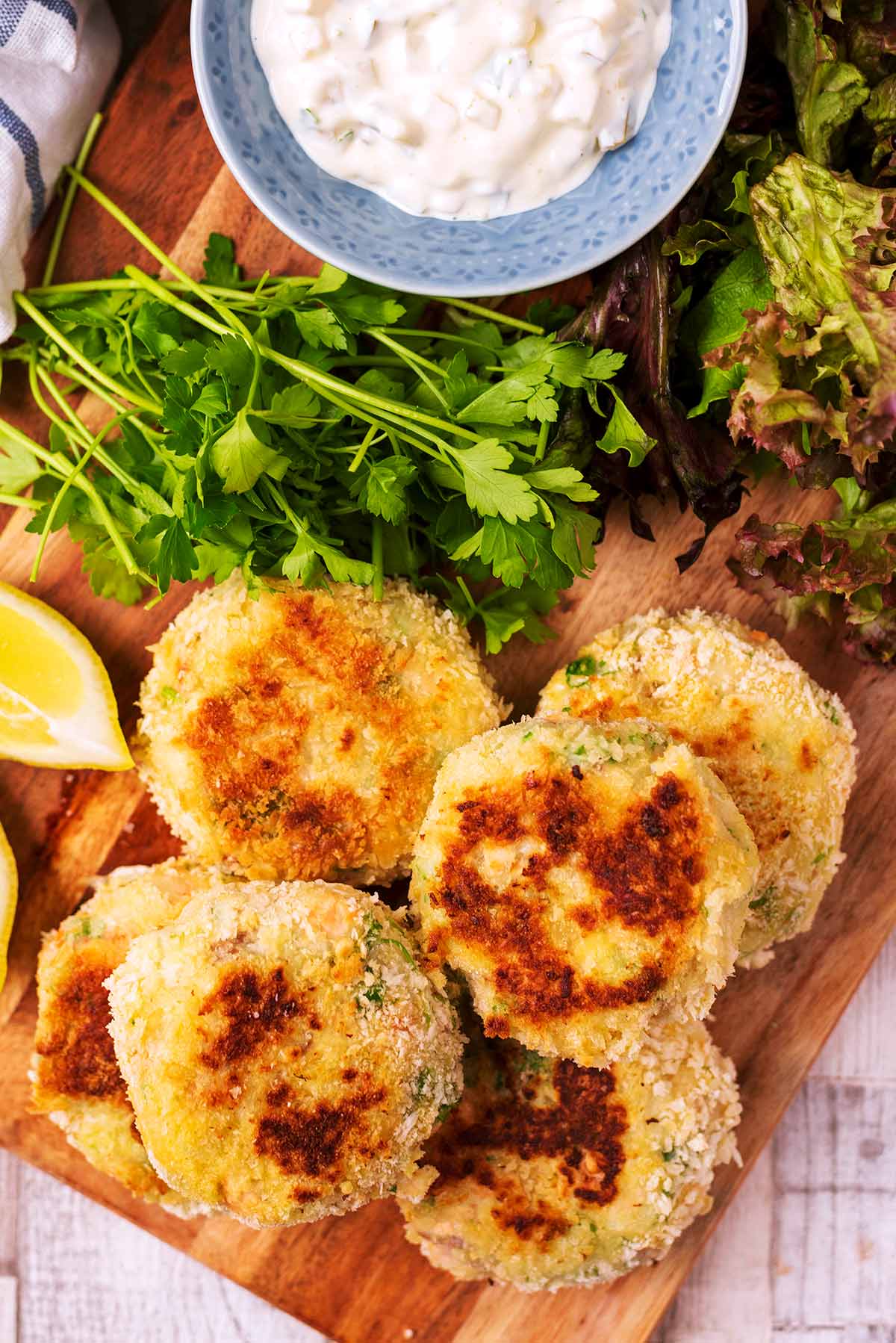 A pile of salmon fishcakes next to some lettuce, coriander and a white creamy dip.