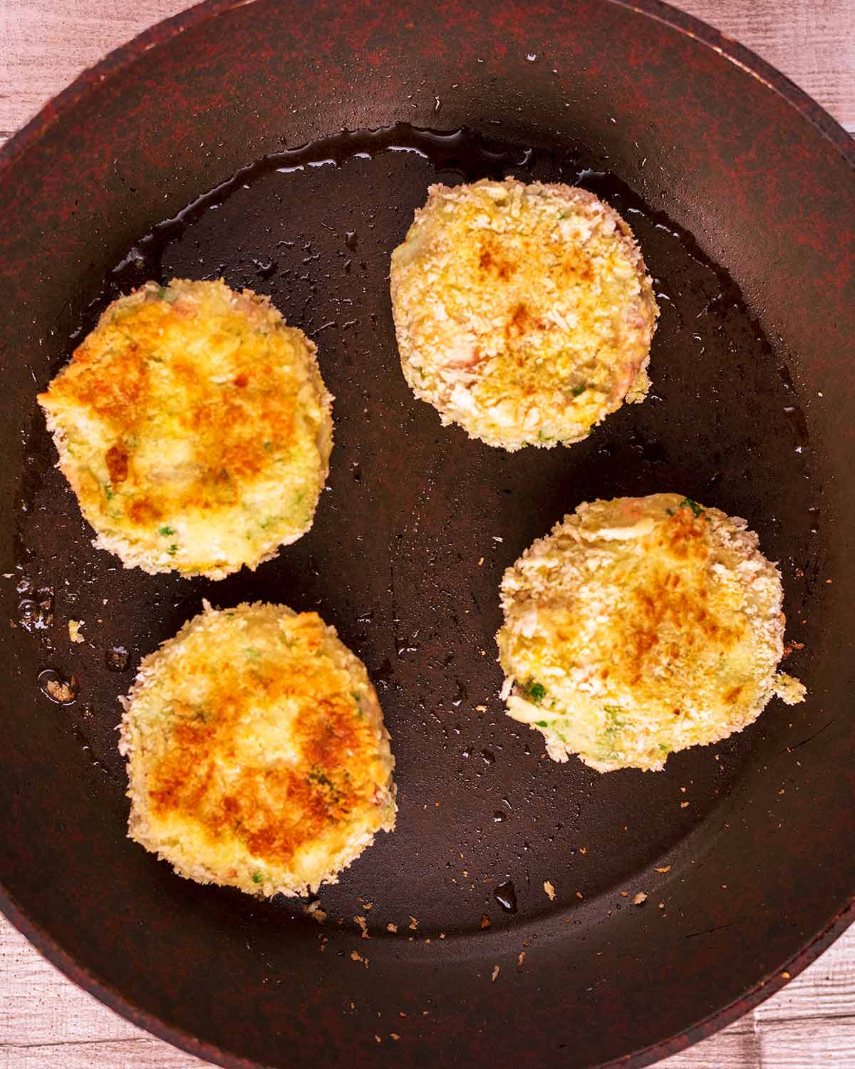 A frying pan with four fishcakes cooking in it.