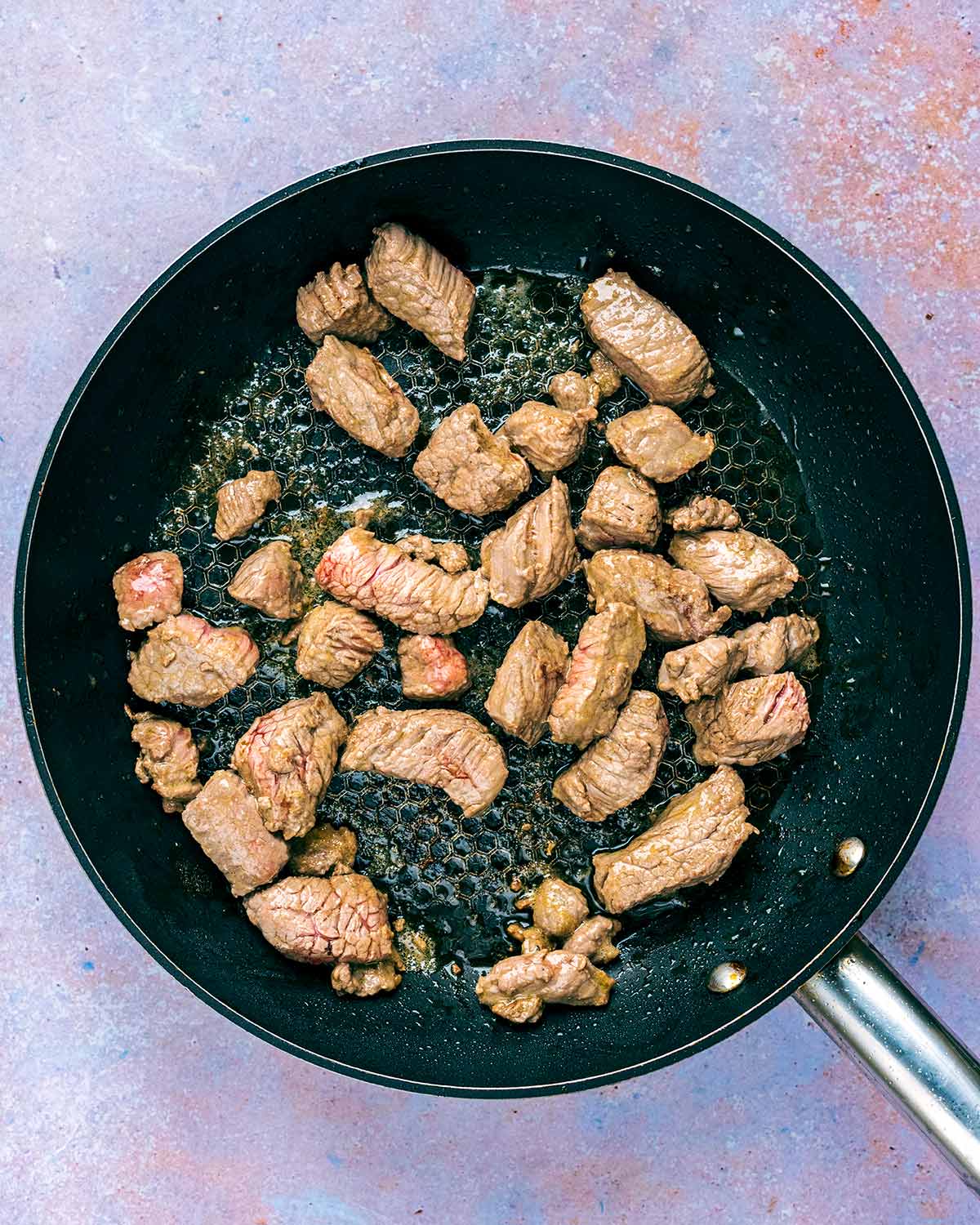 Chunks of beef browning in a frying pan.