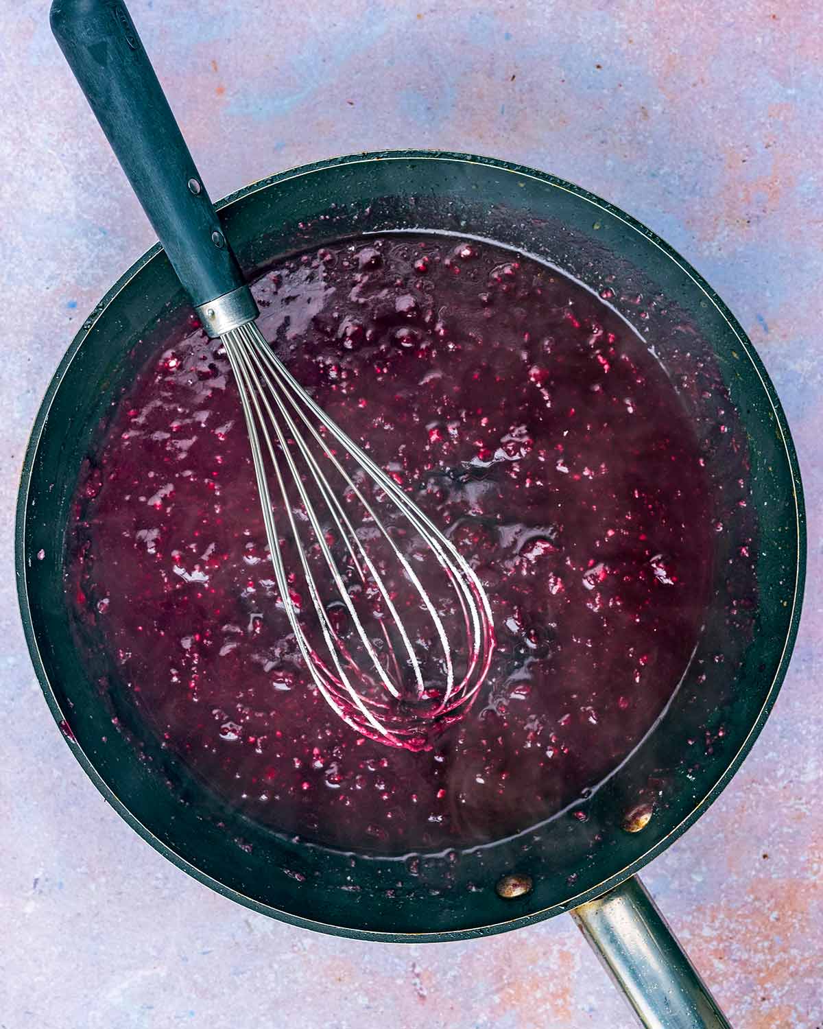 The pan being deglazed with red wine. A whisk is in the pan.