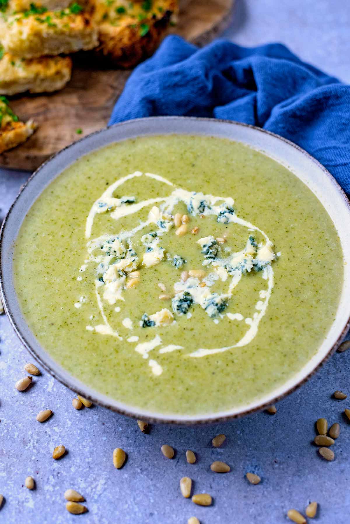 Broccoli and stilton soup in a bowl in front of a blue towel.