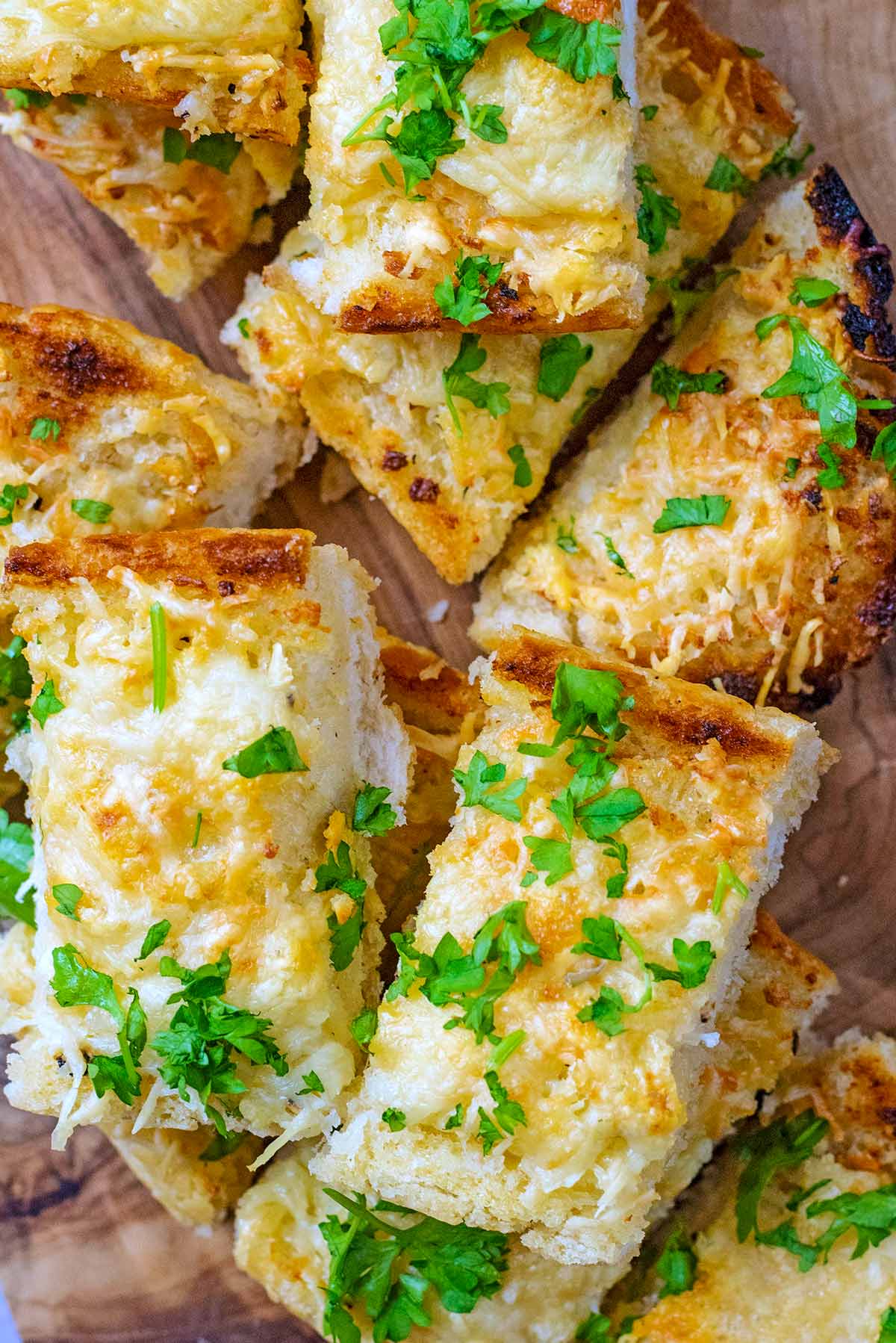 Slices of cheesy garlic bread with chopped herbs sprinkled over them.