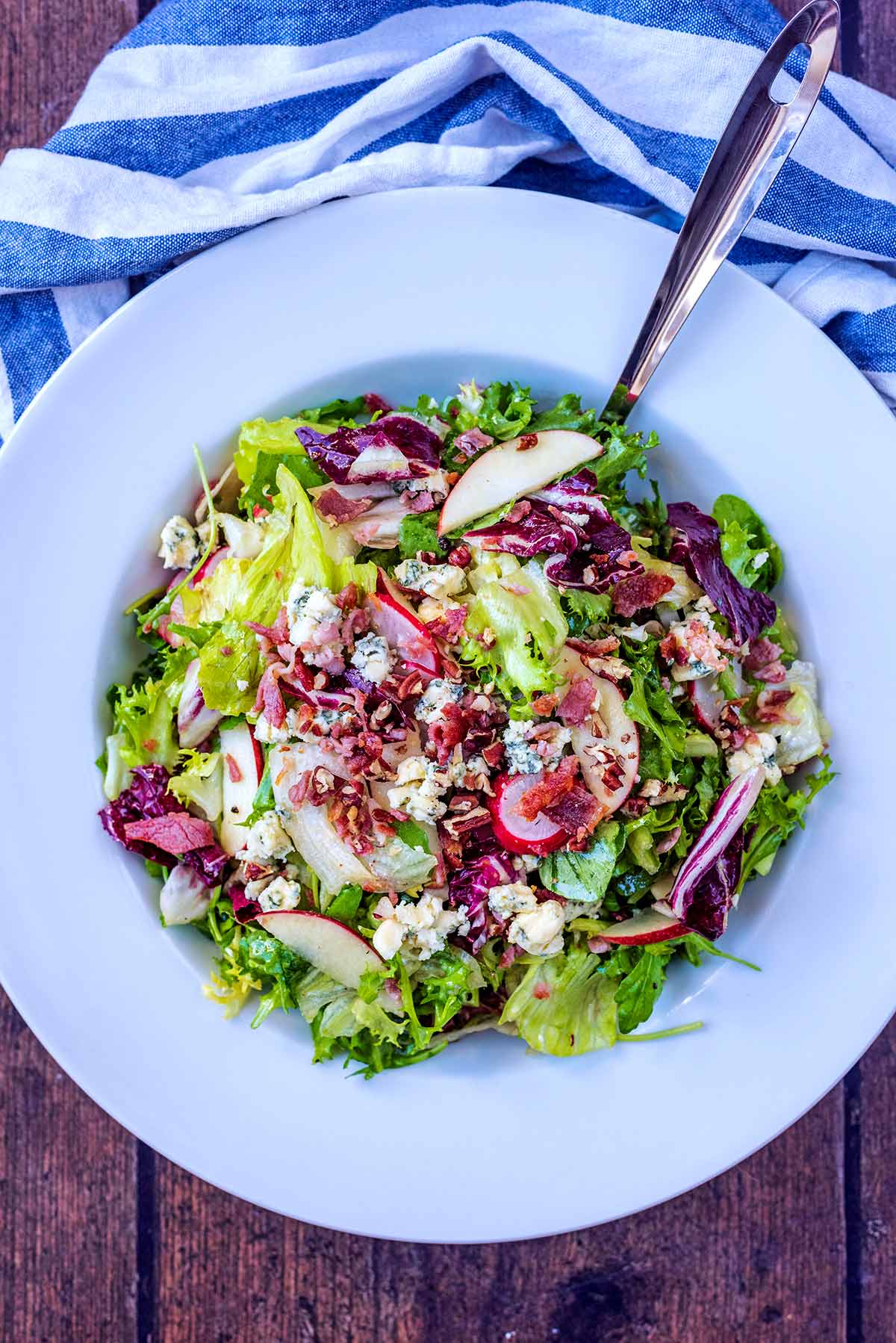 A bowl of salad leaves topped with cheese and bacon.