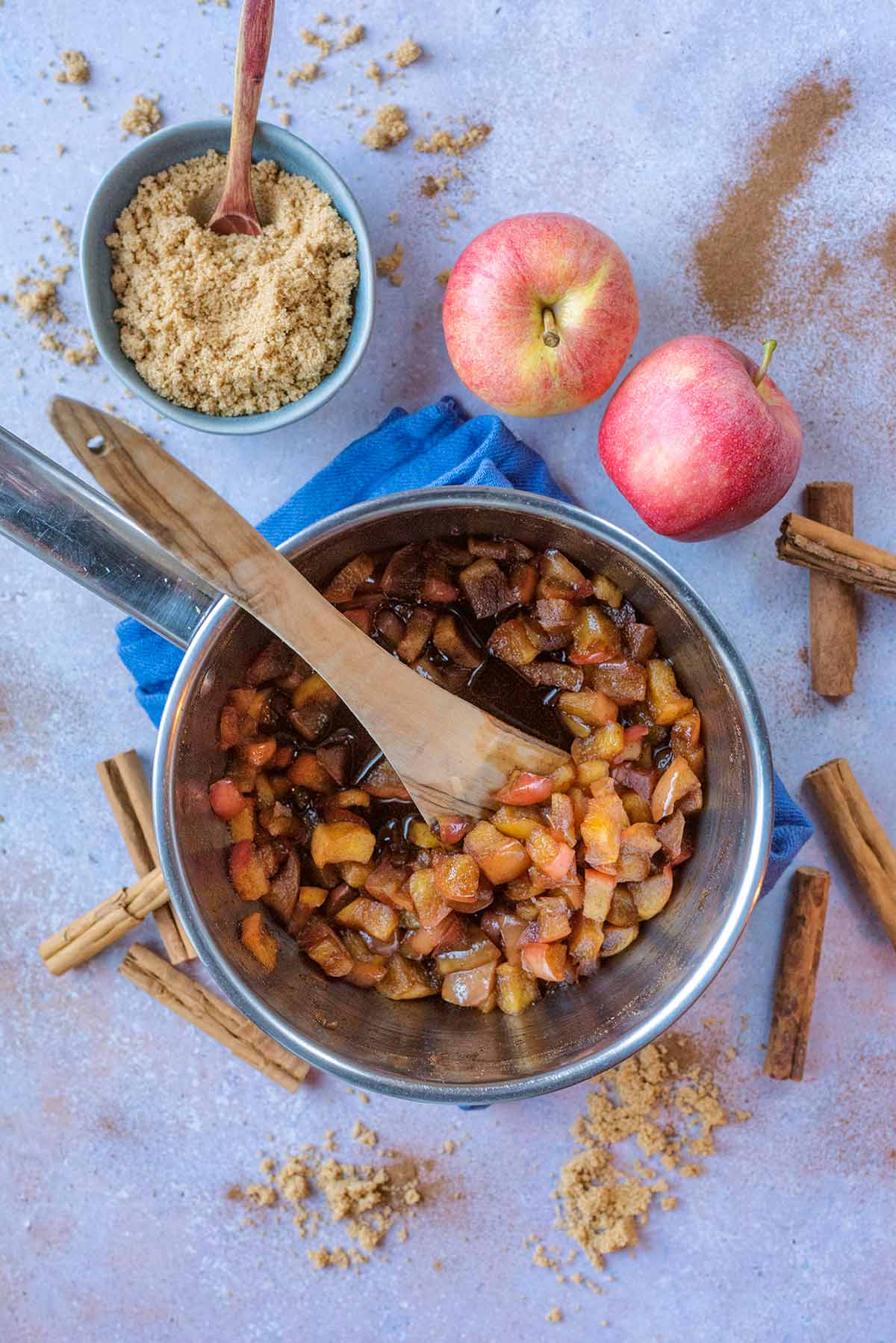 A saucepan containing stewed apples surrounded by apples and cinnamon sticks.