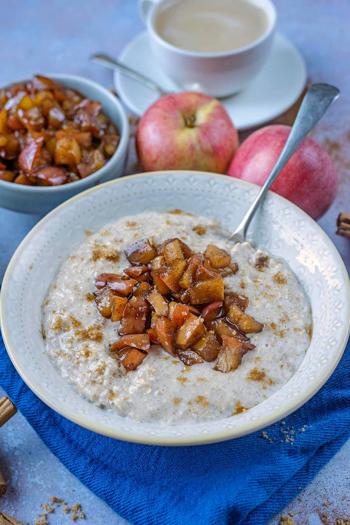 Stewed apples on top of a bowl of porridge with some red apples in the background.