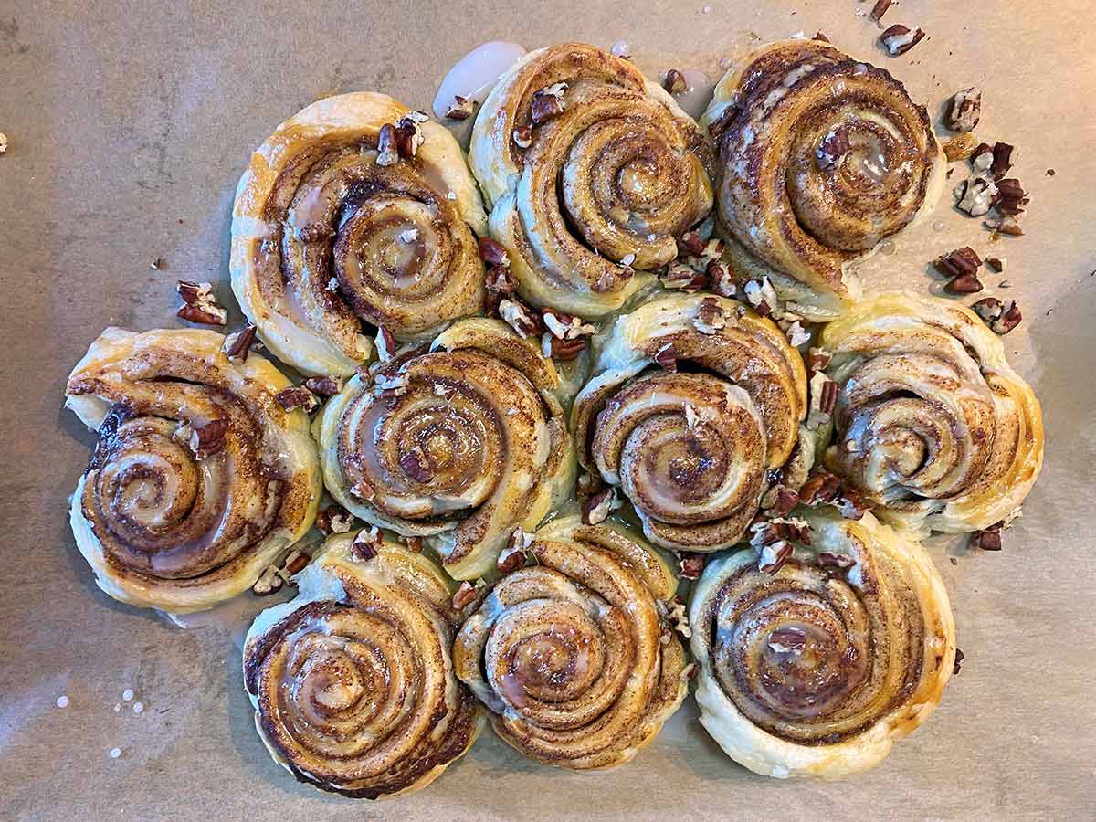 Ten cooked cinnamon swirls topped with icing and chopped pecans.