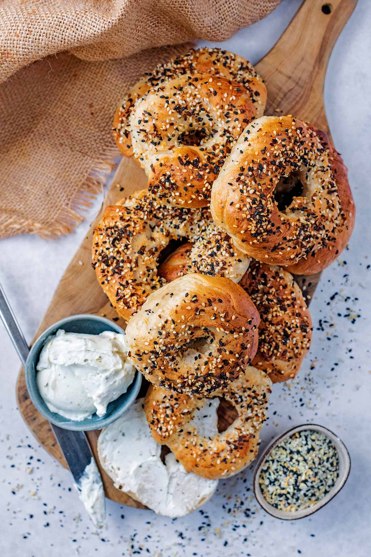 A selection of seeded bagels on a wooden serving board with a small pot of cream cheese.