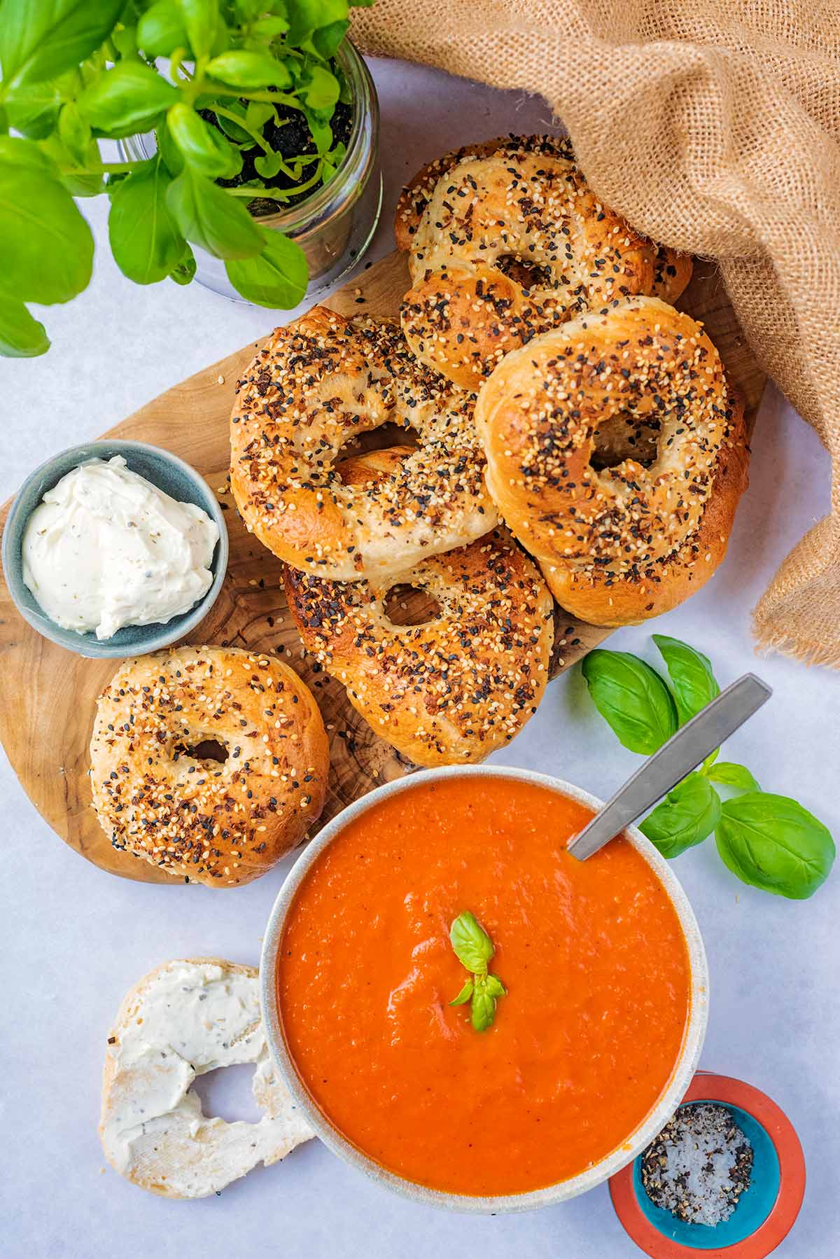 Seeded bagels on a wooden board next to a bowl of tomato soup.