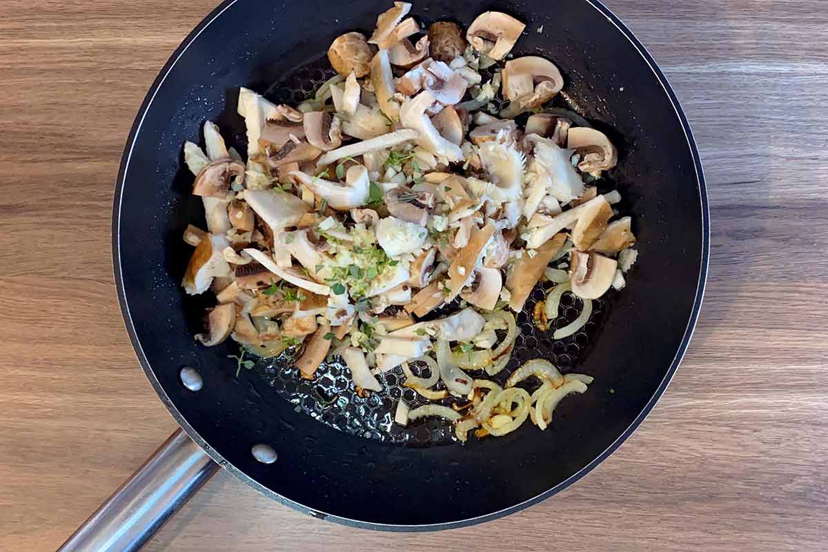 A frying pan containing cooked onions, sliced mushrooms and thyme leaves.