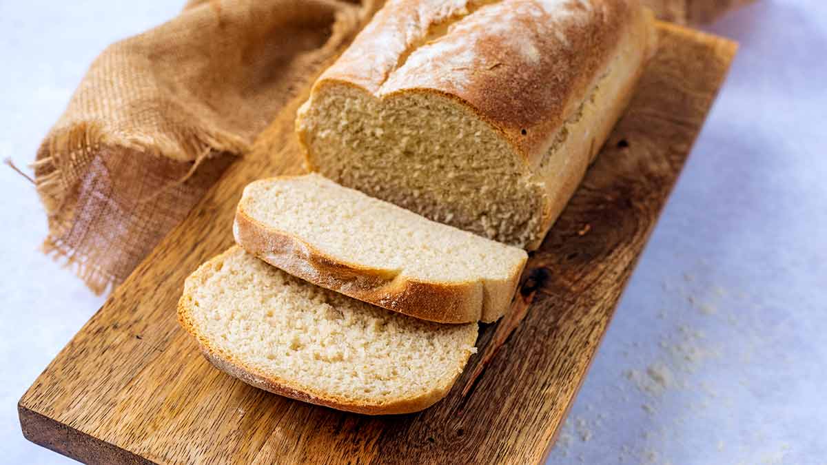 A white loaf on a wooden board with two slices cut off.