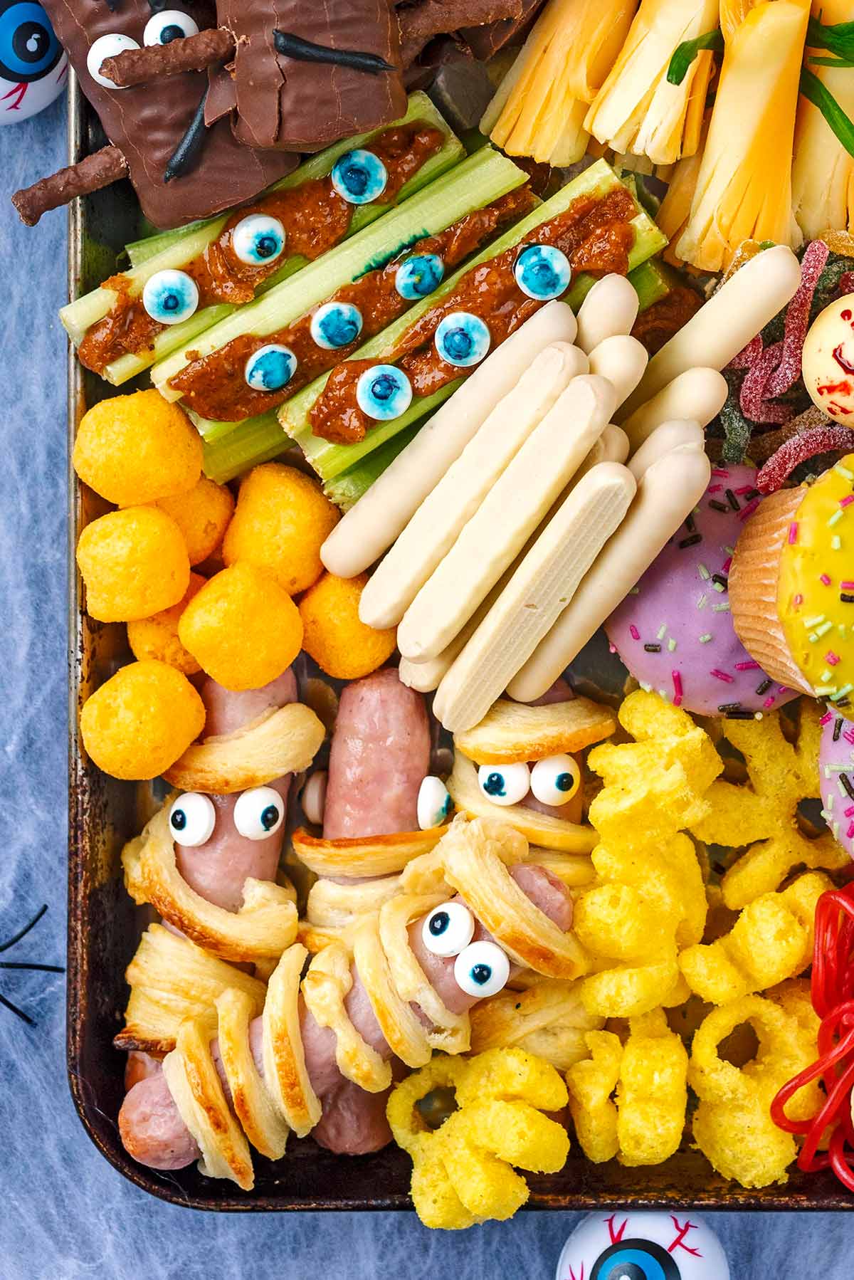 Various sweet treats set out on a platter, including sausage mummies, zombie celery sticks, monster munch and white chocolate fingers.