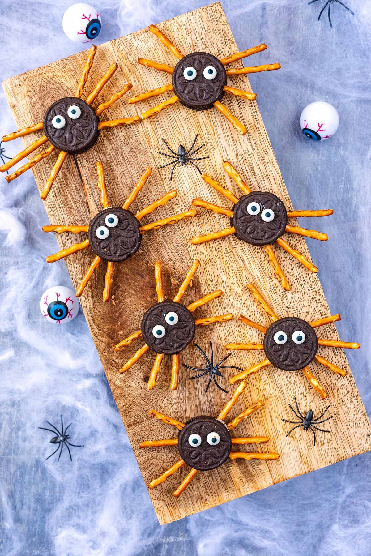A wooden serving board with seven Oreo cookies decorated like spiders.