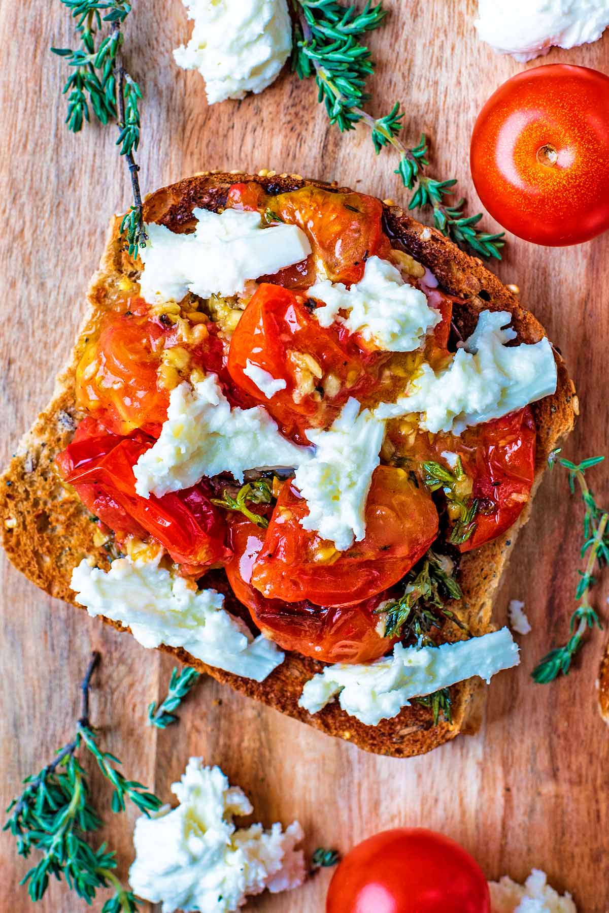 A slice of toast topped with Roasted Cherry Tomatoes, cheese and thyme.