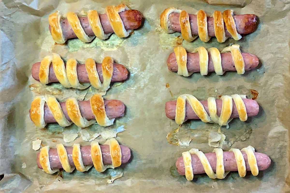 Eight cooked pastry wrapped sausages on a lined baking tray.