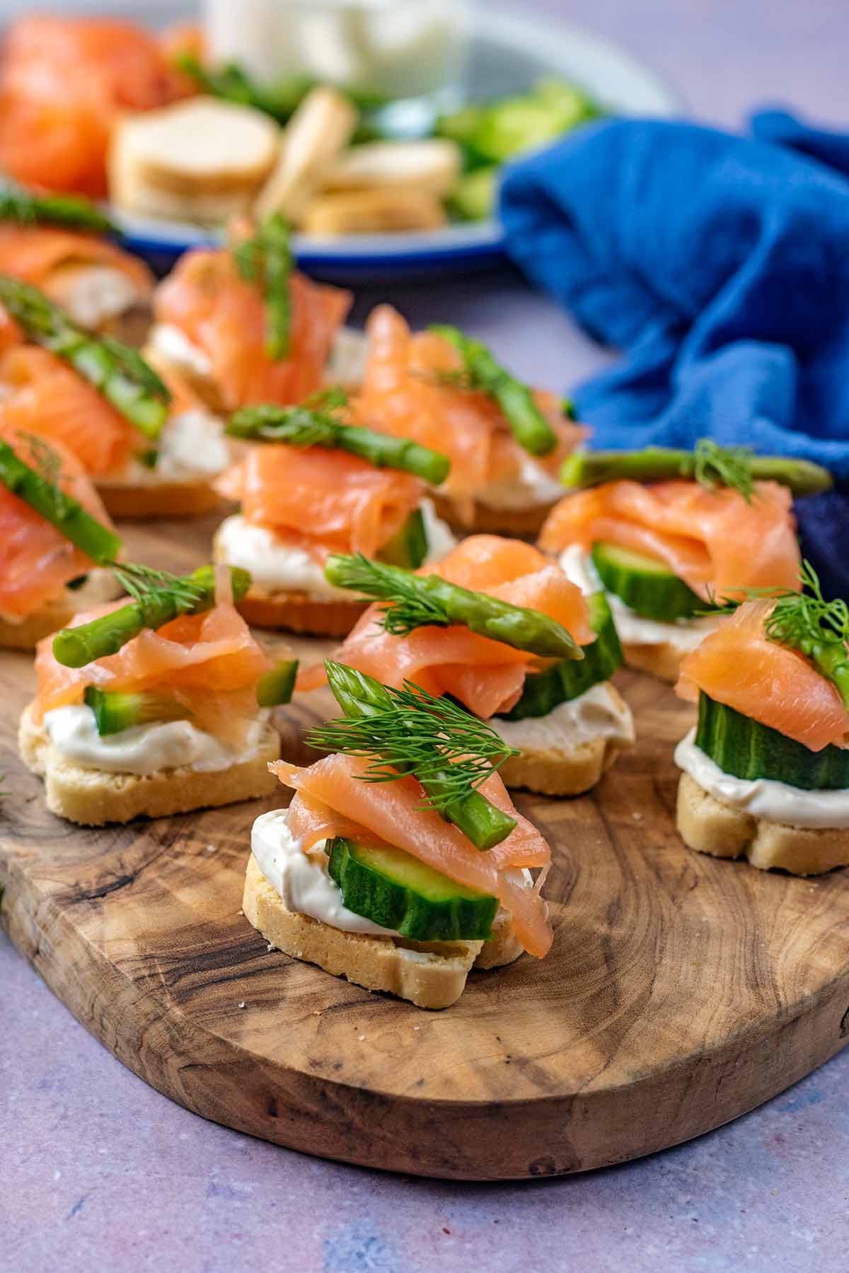 Salmon canapes on a wooden board in front of a blue towel.