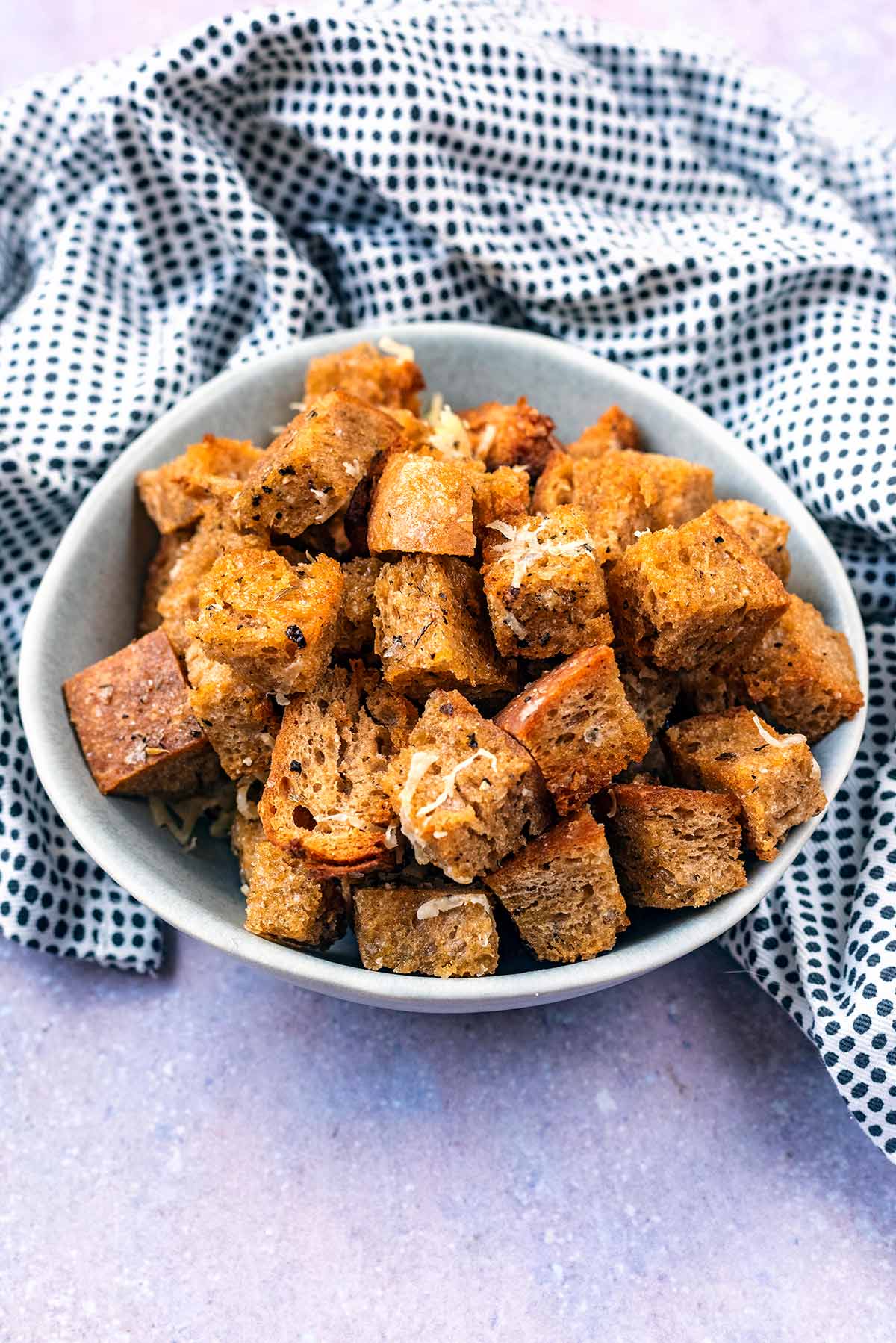 A bowl of croutons in front of a spotted towel.
