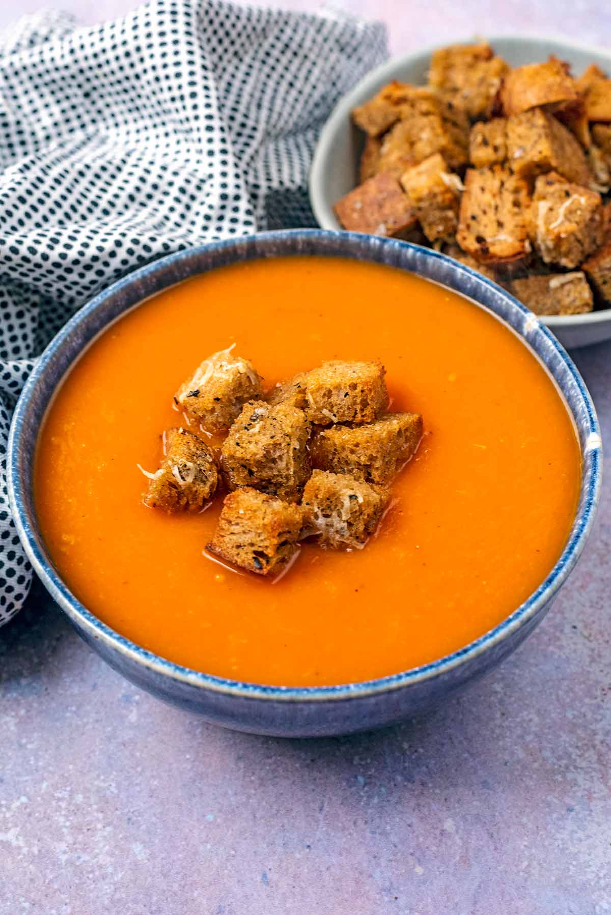 A bowl of tomato soup with some croutons on the top of it.