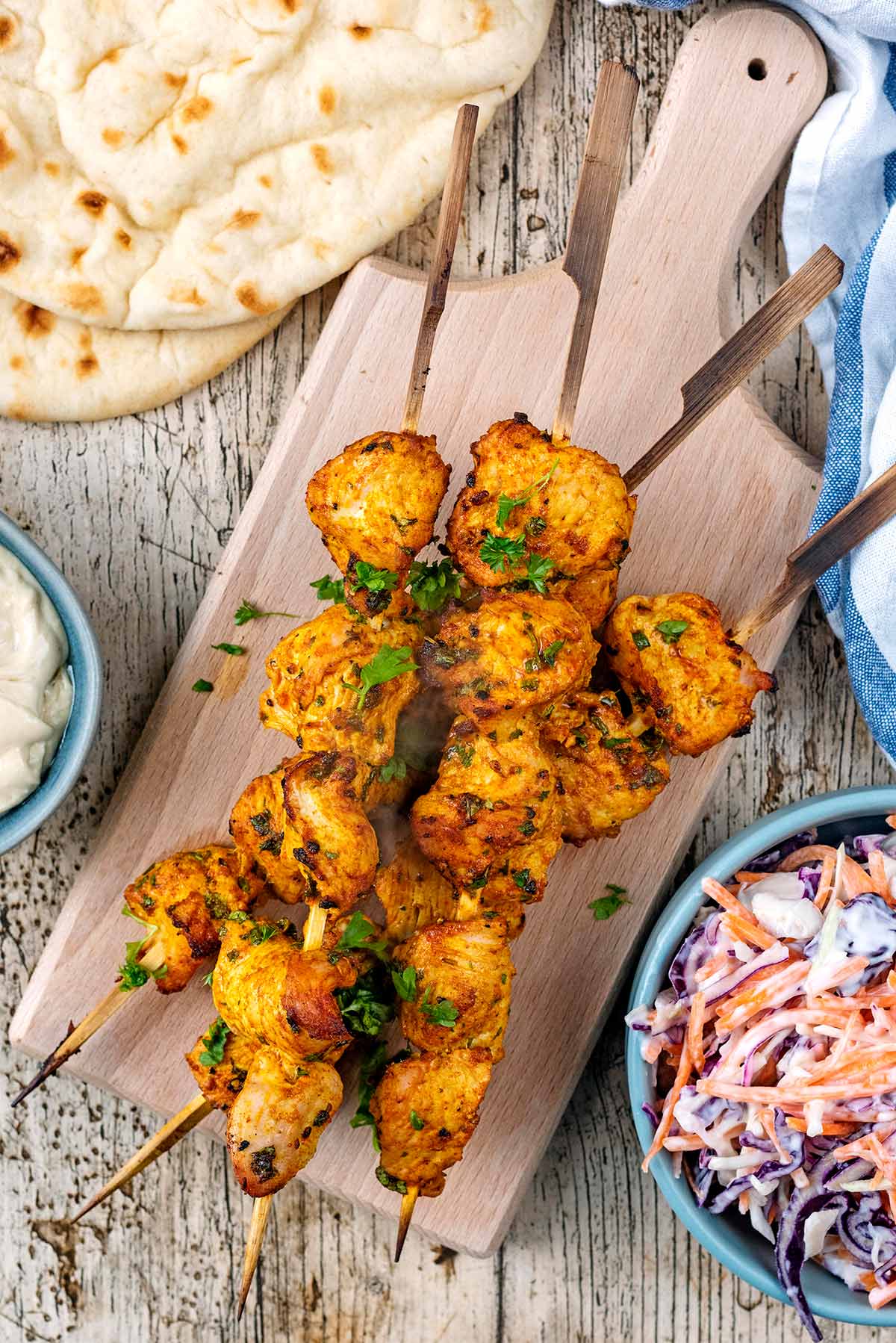 Four turkey kebabs on a wooden serving board next to flatbreads, slaw and dip.