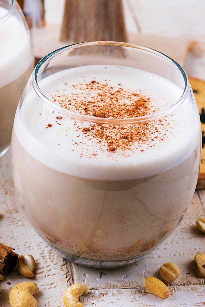 A glass full of eggnog topped with a sprinkling of cinnamon.