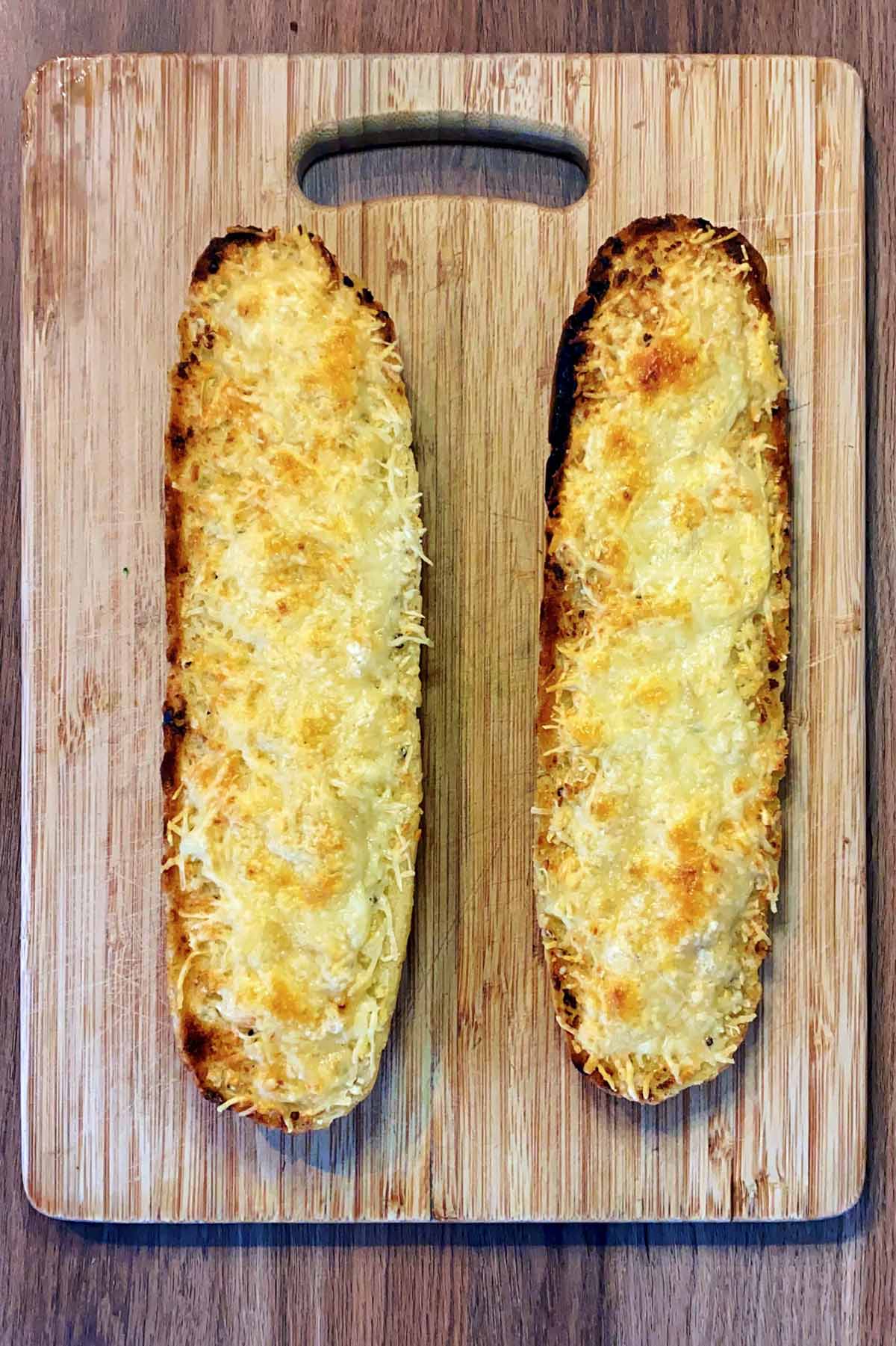 Cooked cheesy garlic bread on a chopping board.
