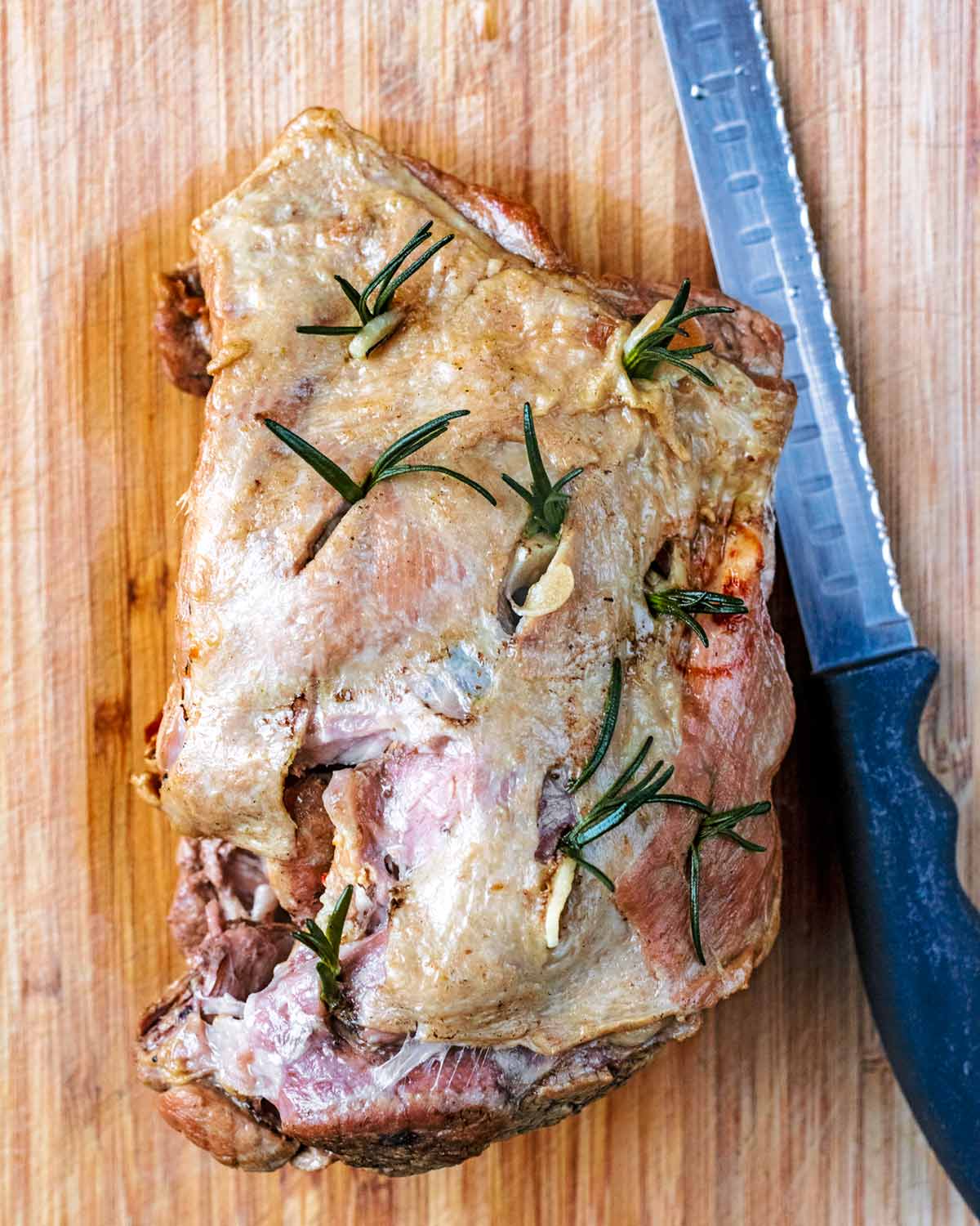 Cooked lamb shoulder on a chopping board with a carving knife.