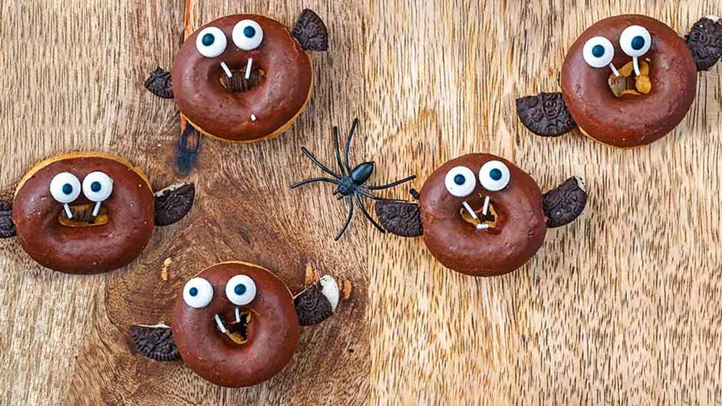 Five Halloween doughnut bats on a wooden surface.