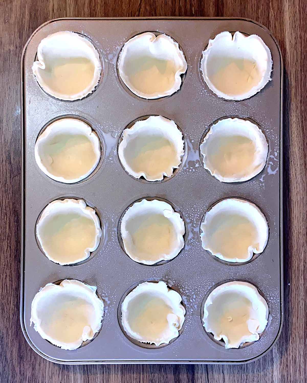 The pastry disks pressed into a muffin tin.