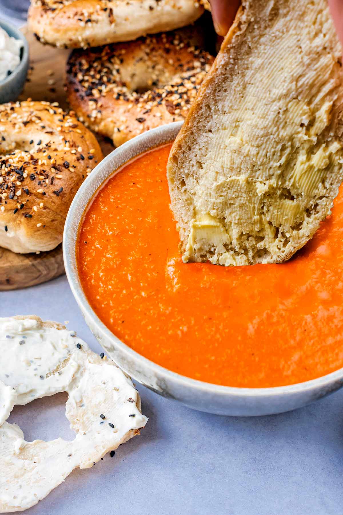A slice of buttered bread being dipped into a bowl of tomato soup.