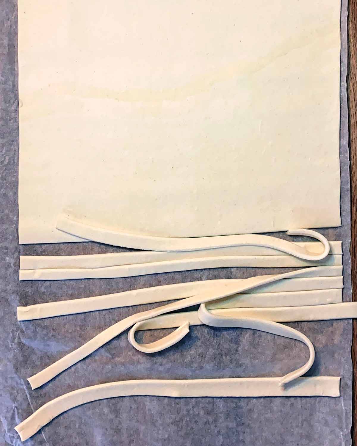 A sheet of puff pastry with thin strips cut off of it.
