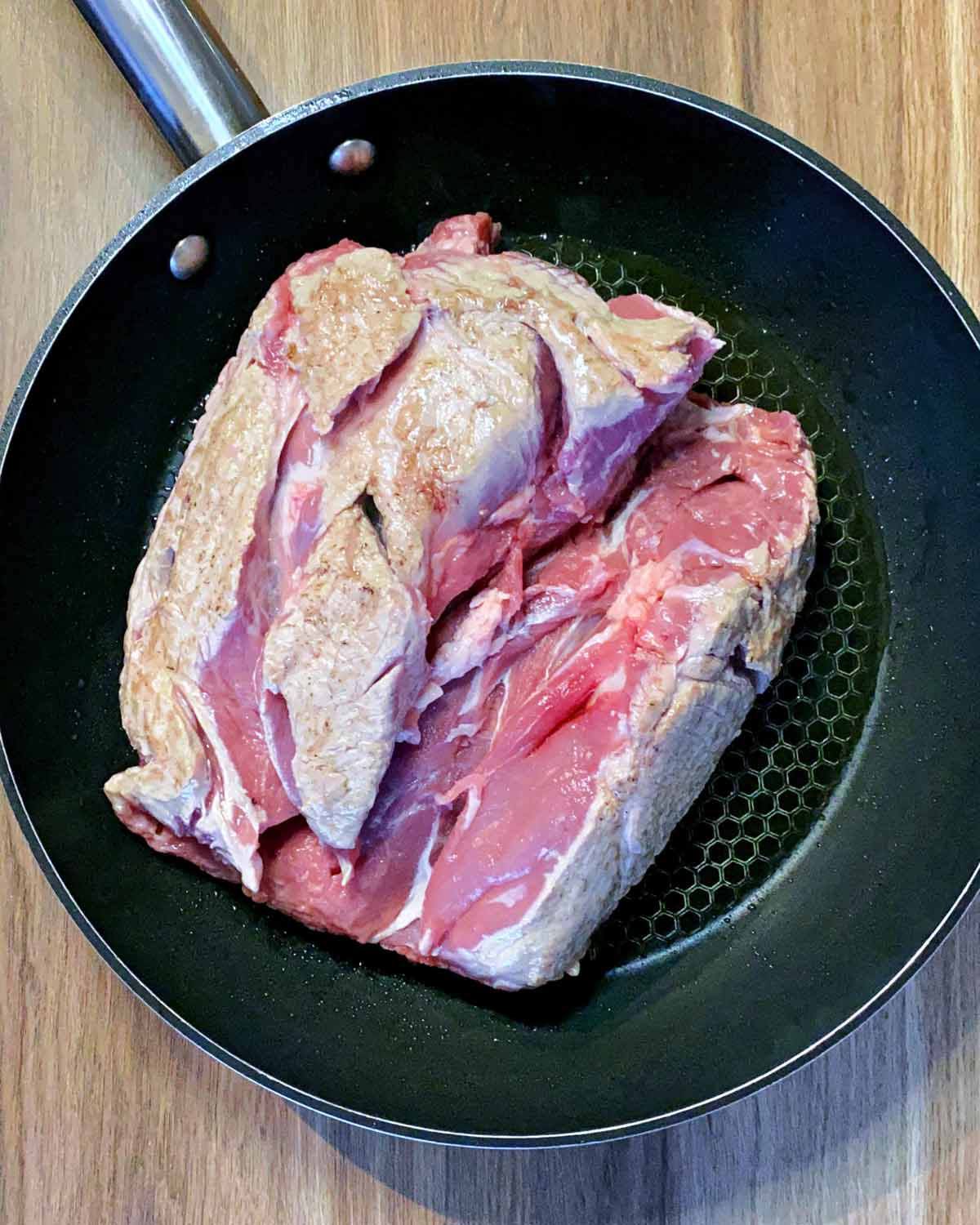 A whole lamb shoulder in a frying pan.